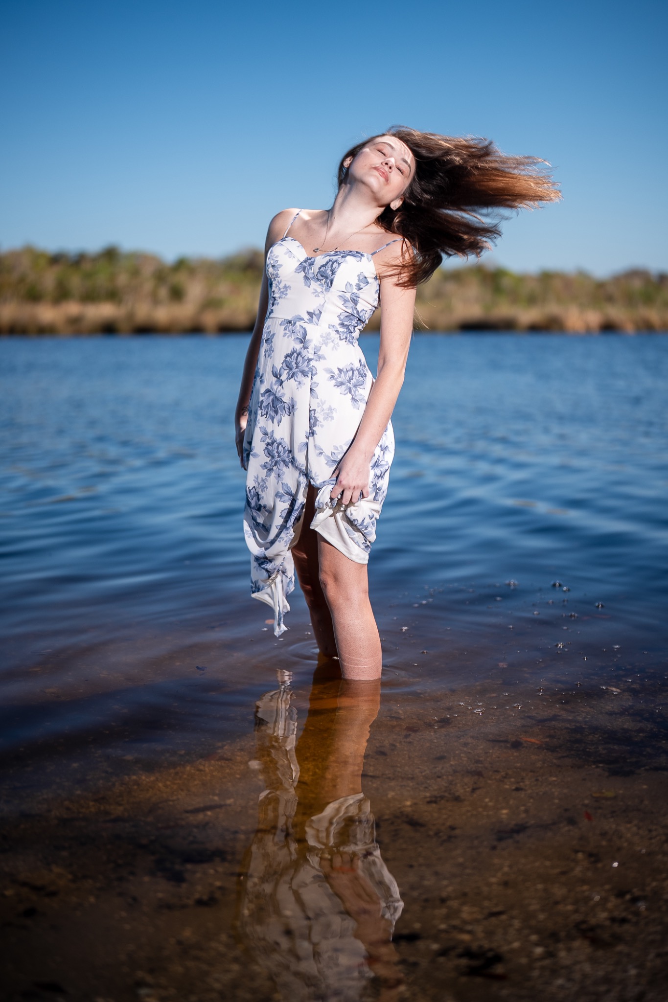Senior portrait of a young woman standing in the Intracoastal, hair sweeping through the air in bright afternoon light