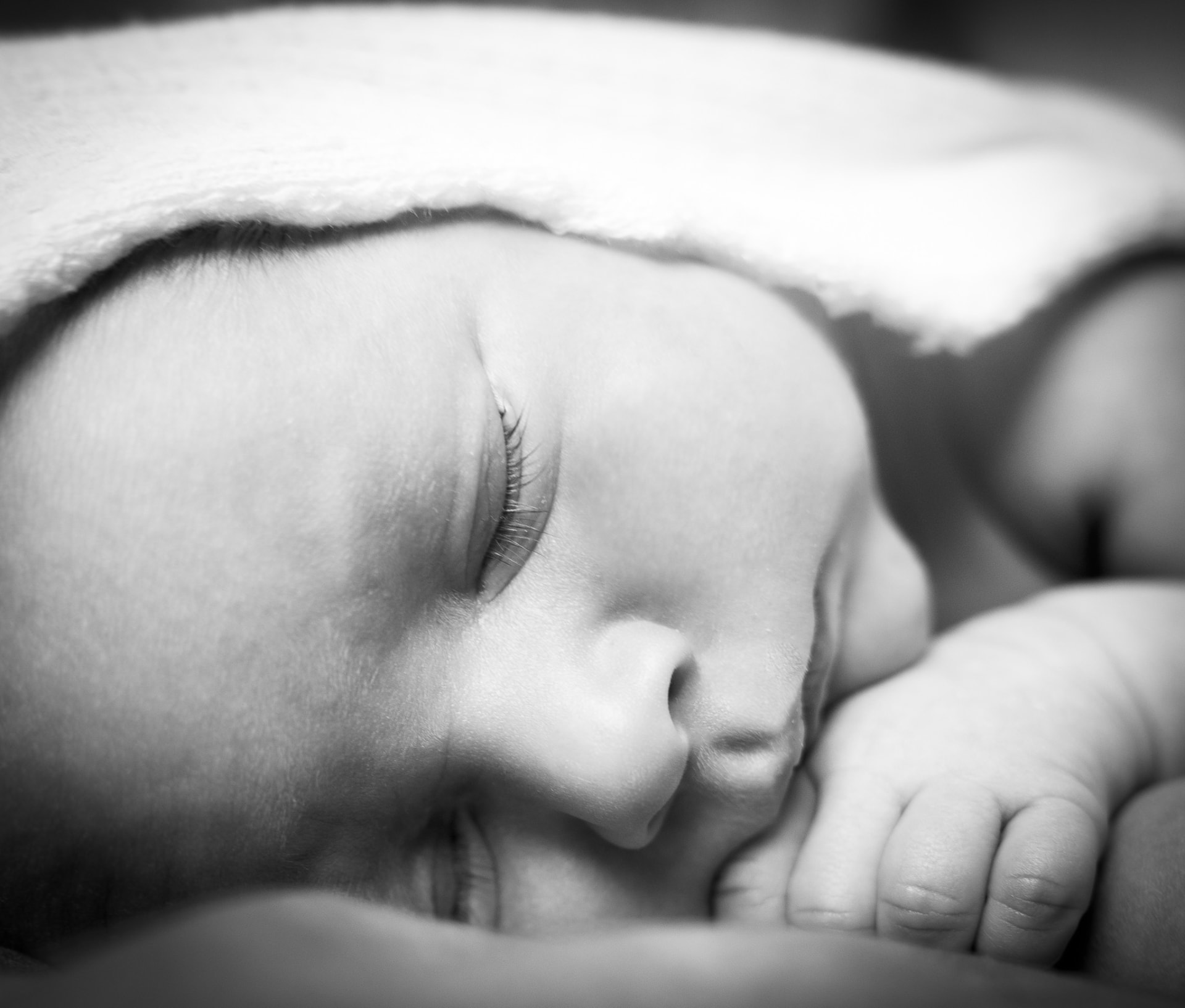 Close-up black-and-white portrait of a sleeping newborn resting on folded hands