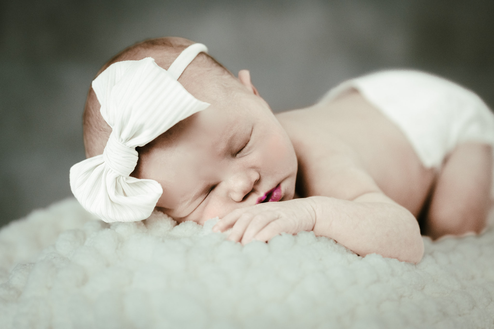 Sleeping newborn wearing a cream bow, resting on a fluffy mint blanket