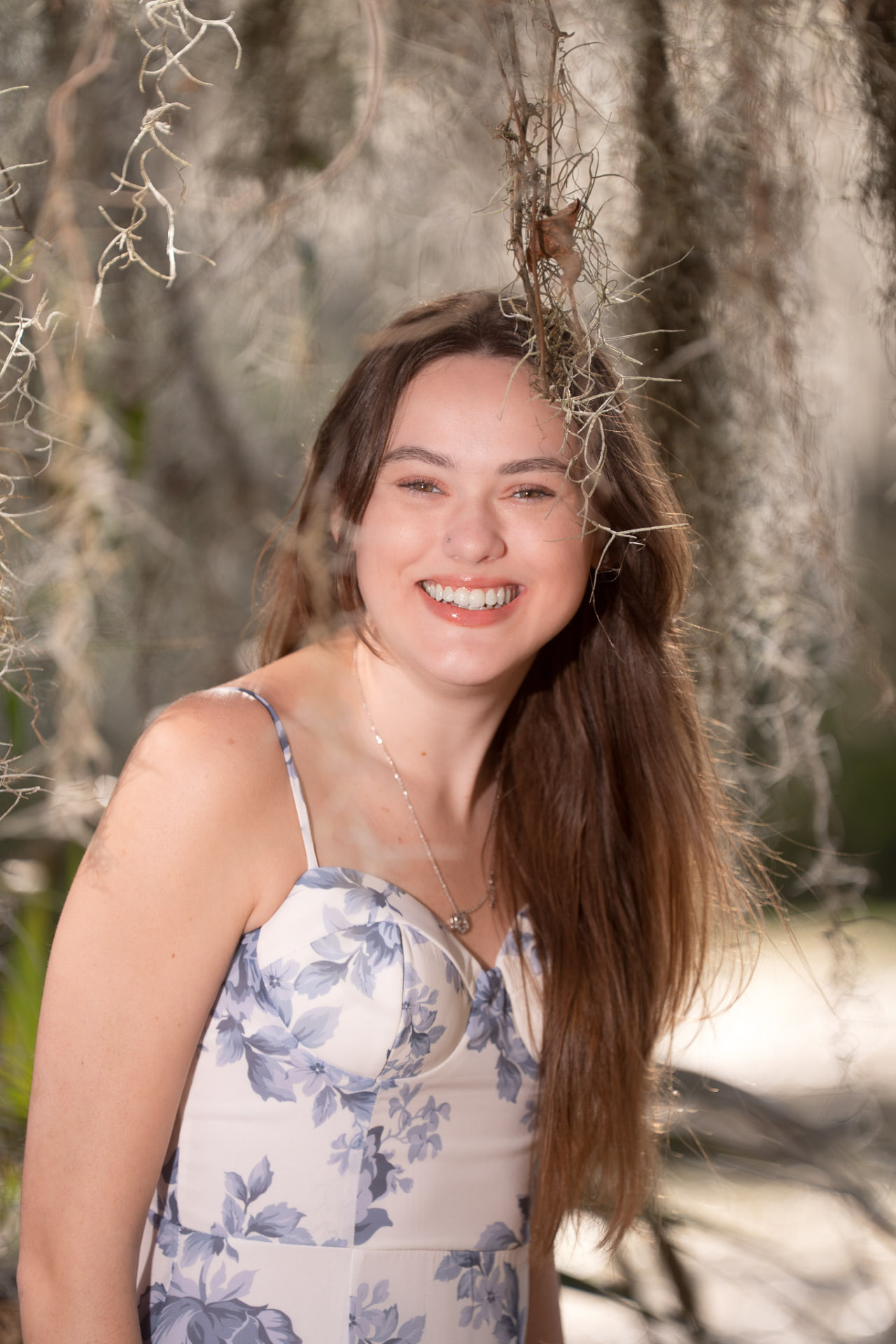 Smiling young woman in a blue floral dress beneath draping Spanish moss