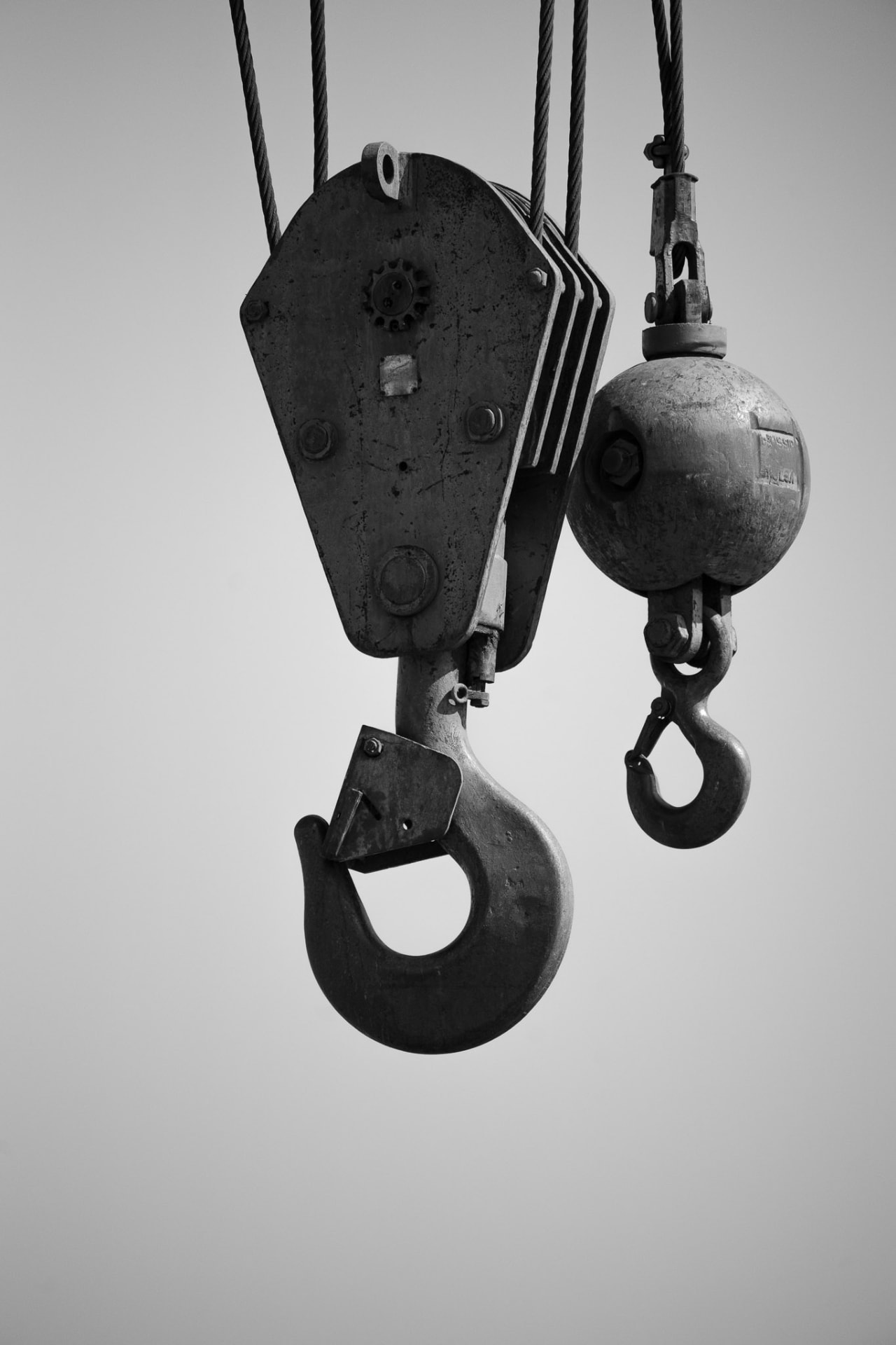 Industrial crane hook and ball hanging against a bright sky, weathered metal and cable rigging in black and white