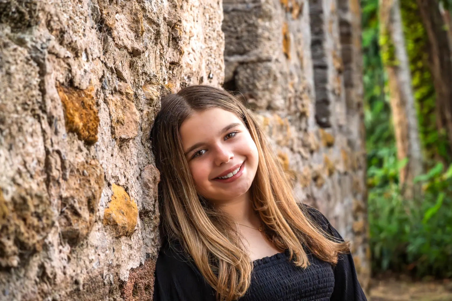 Young girl smiling while leaning against a weathered coquina stone wall