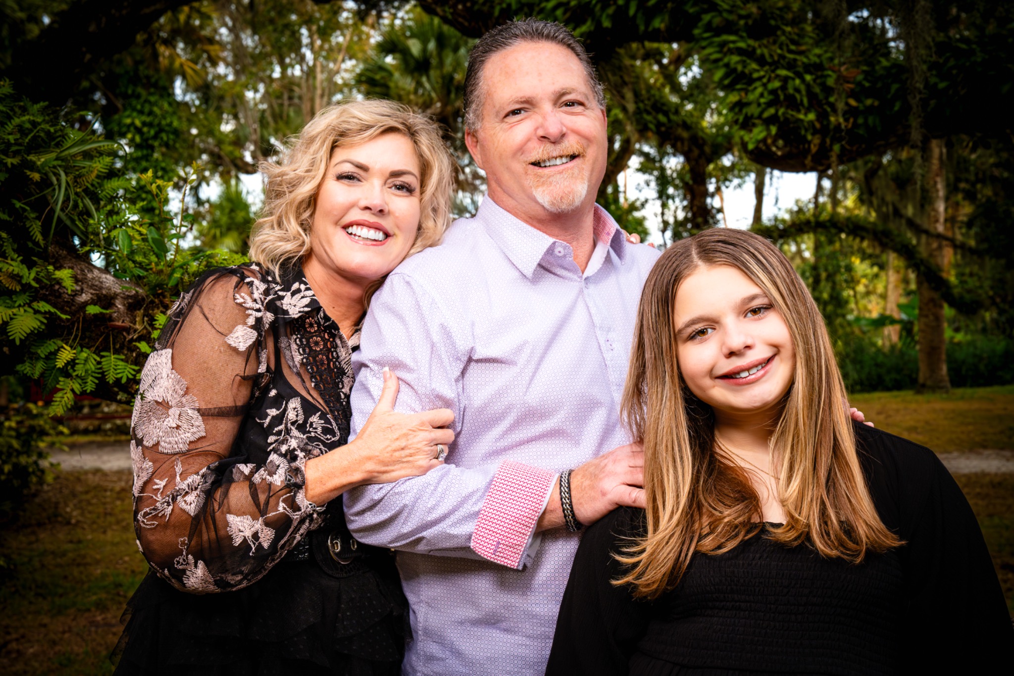Family of three embracing and smiling beneath live oaks draped in Spanish moss
