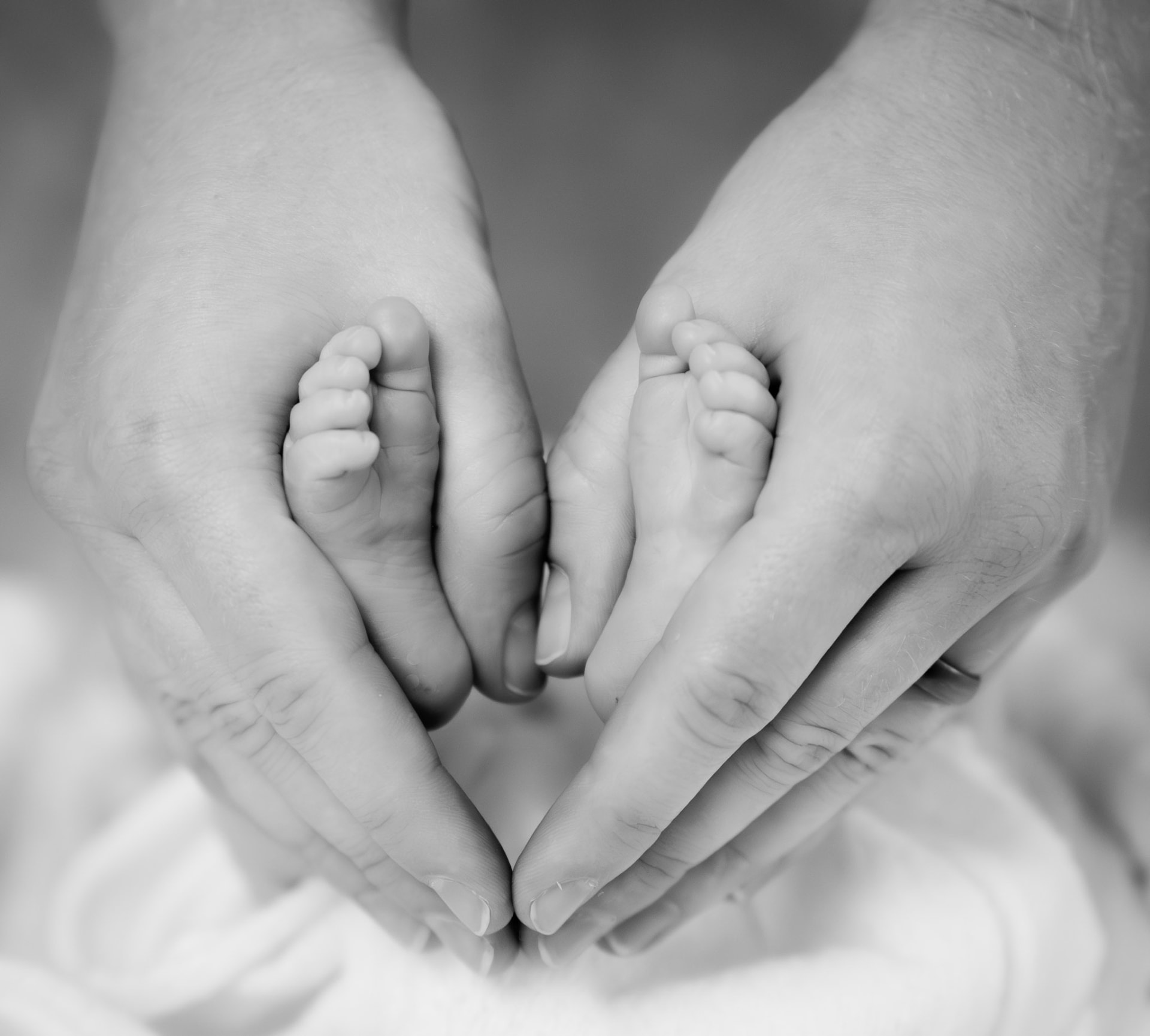 Black-and-white close-up of adult hands gently cradling newborn feet in a heart shape