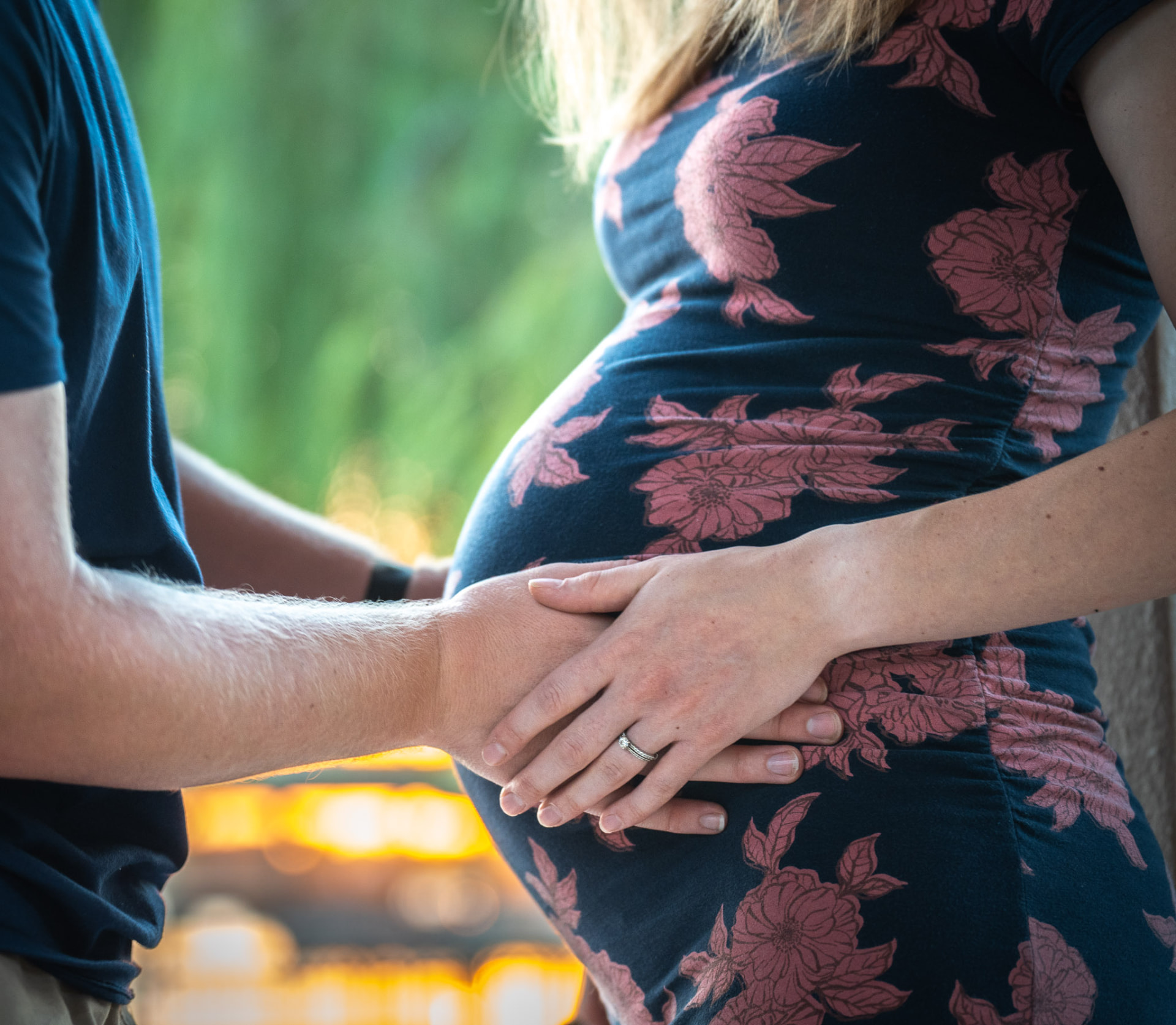 Close-up of a couple's hands resting together on a pregnant belly, the woman in a navy dress with pink florals