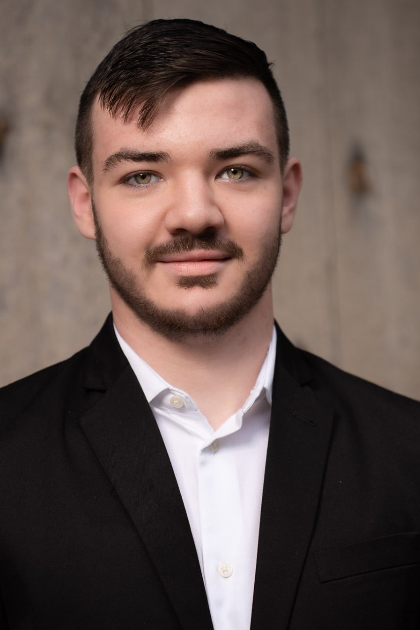 Senior portrait of a young man in a black suit and white shirt in front of a weathered wooden door