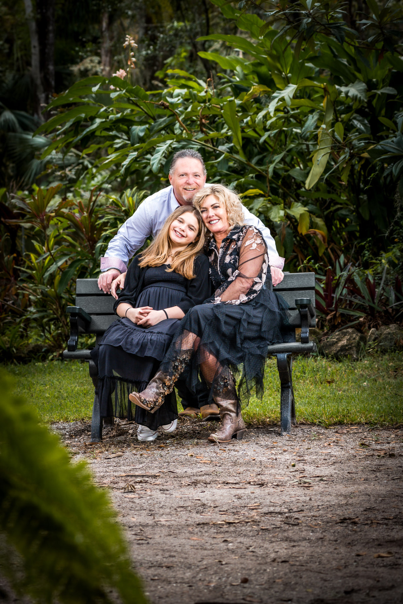 Parents and their daughter seated together on a garden bench surrounded by lush tropical greenery