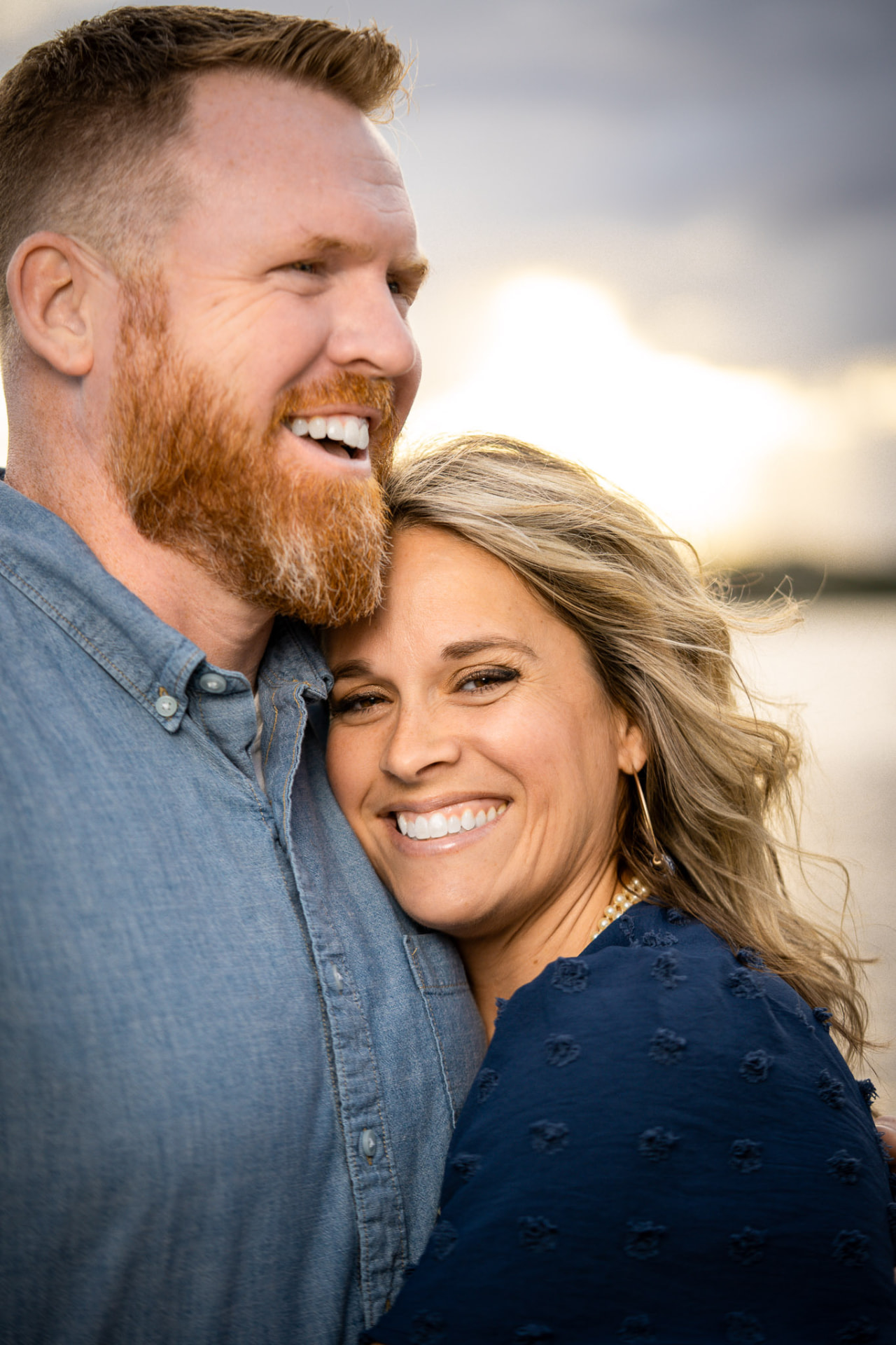 Couple laughing together at sunset, the woman resting her head on the man's shoulder in golden coastal light