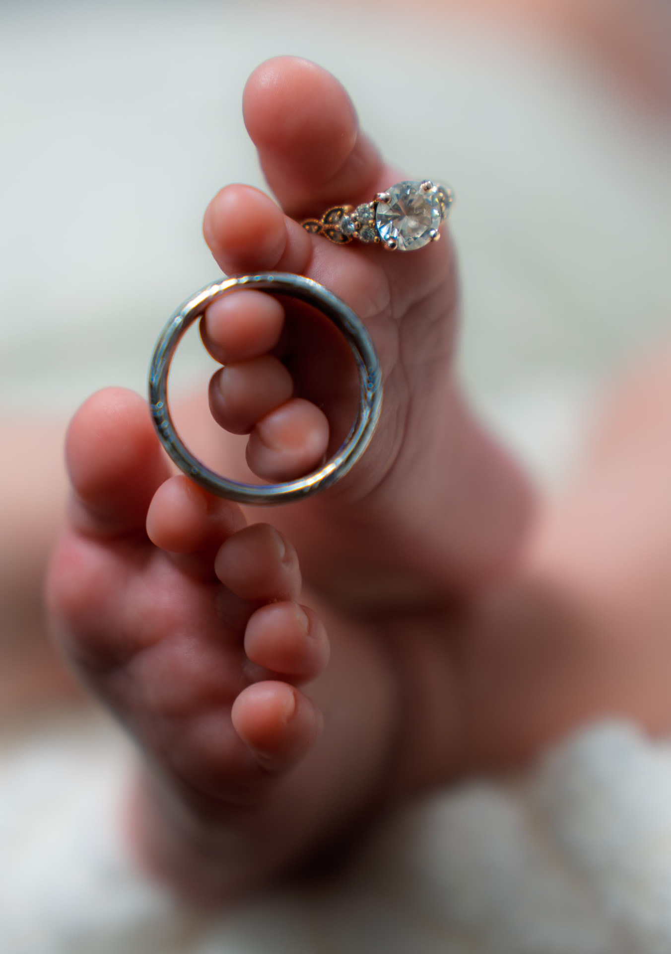 Close-up of a newborn's tiny feet with the parents' wedding rings resting on the toes