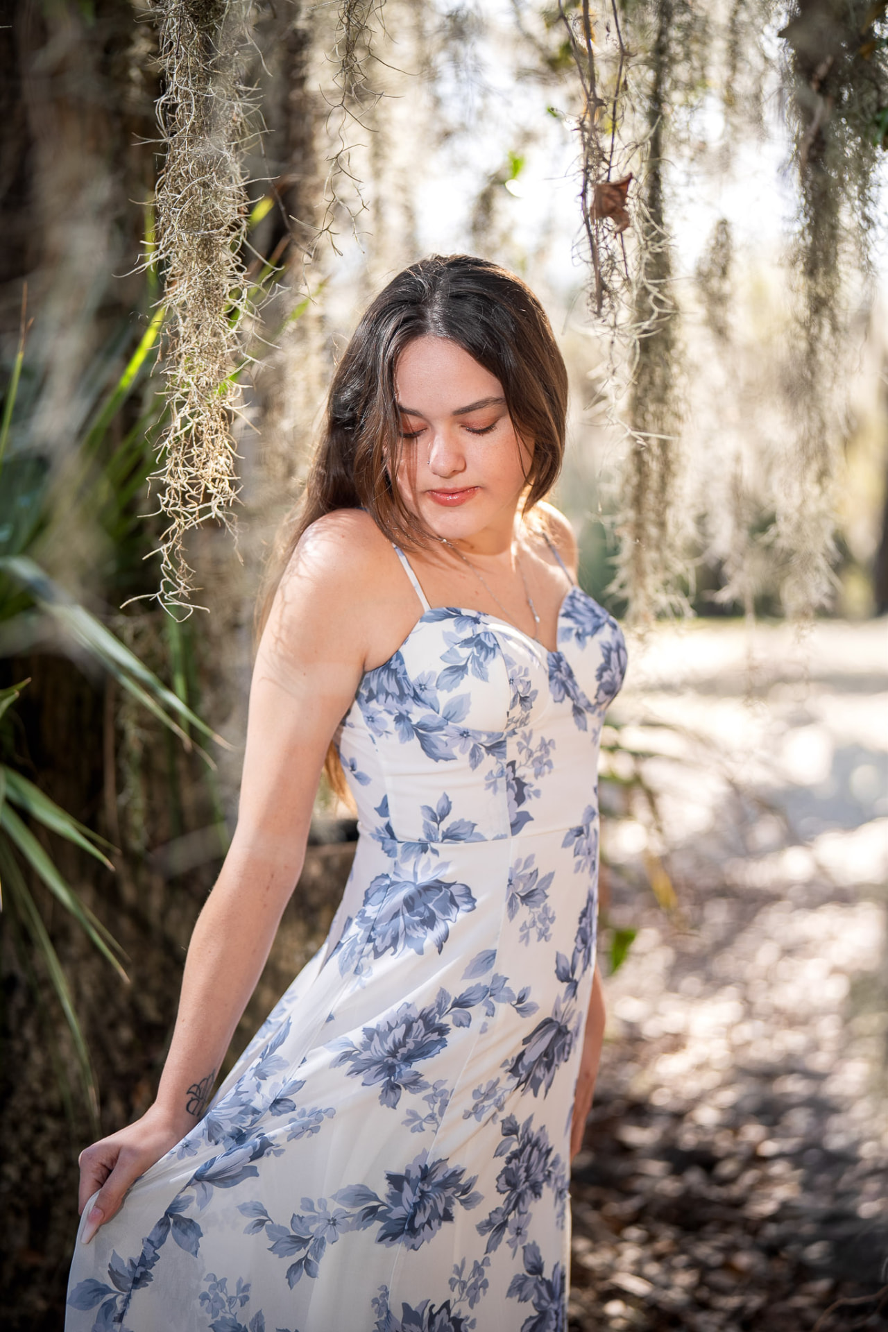 Young woman in a blue floral dress standing on a path framed by Spanish moss and live oaks