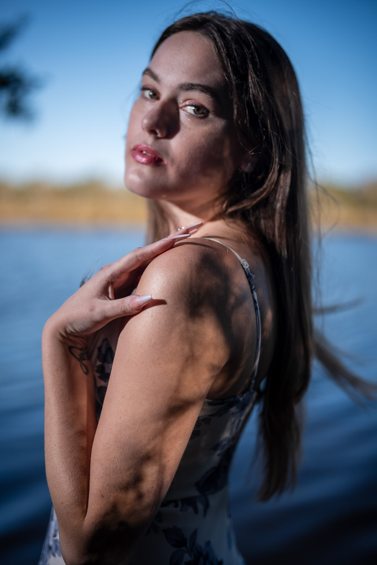 Young woman in a floral dress glancing over her shoulder against deep blue water at dusk