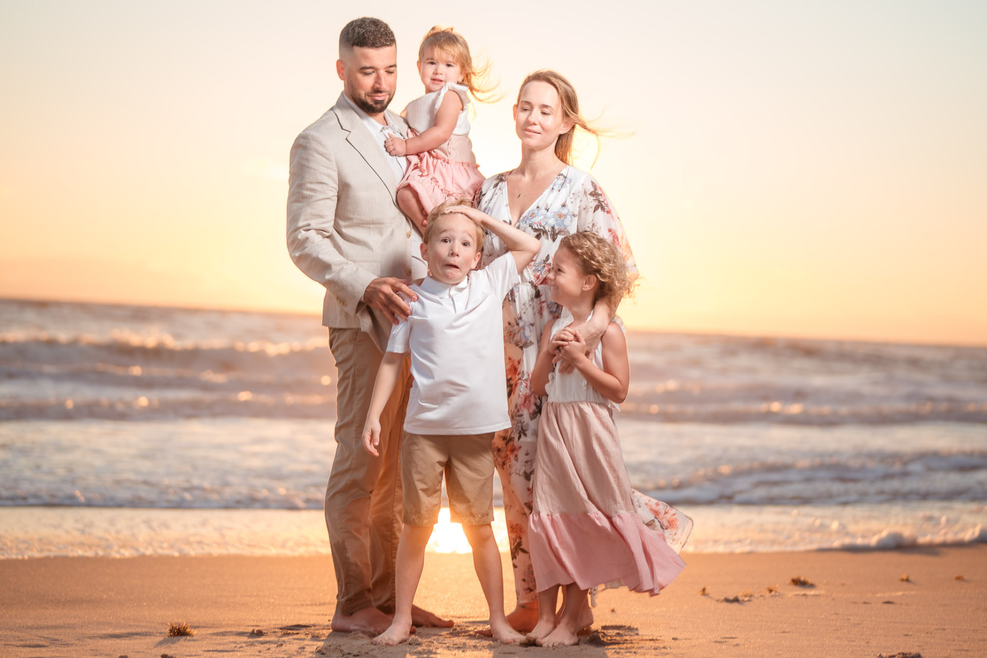 Family of five standing together on the beach at golden sunset, waves glowing behind them